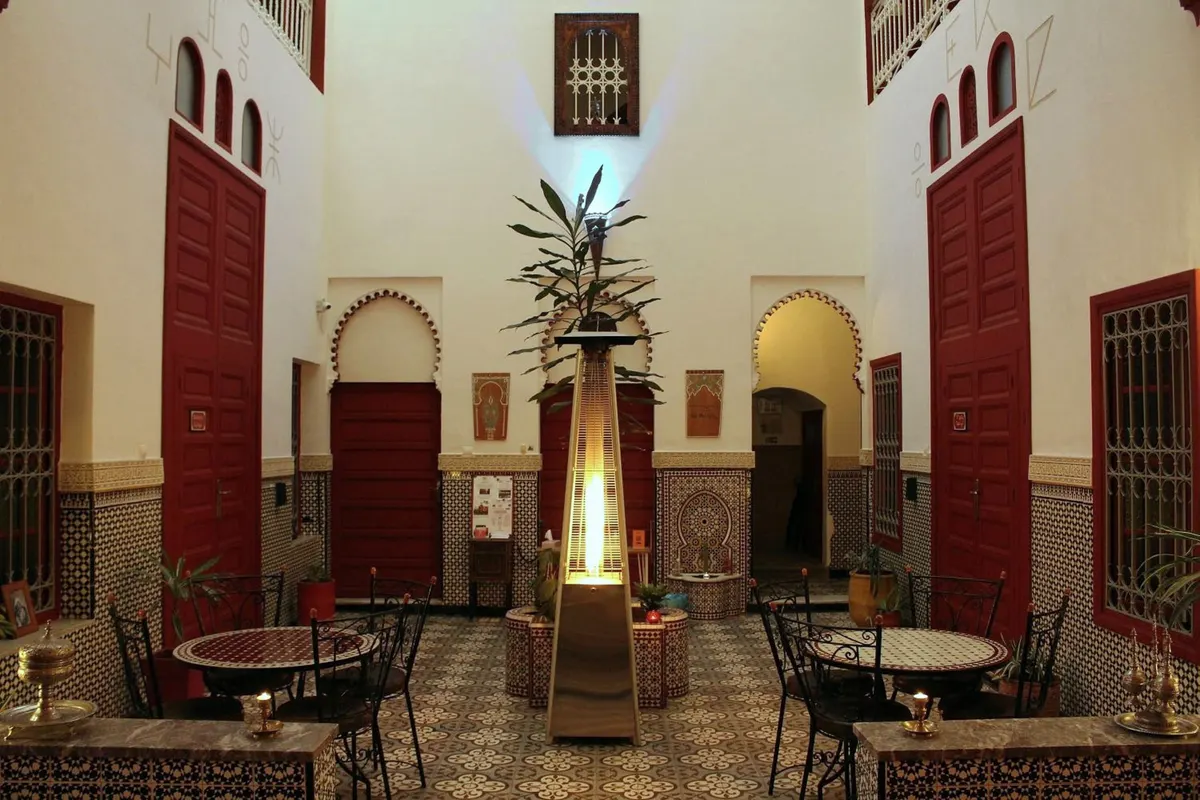 El patio central: puertas rojas de cedro, arcos de herradura, zellige y mesas