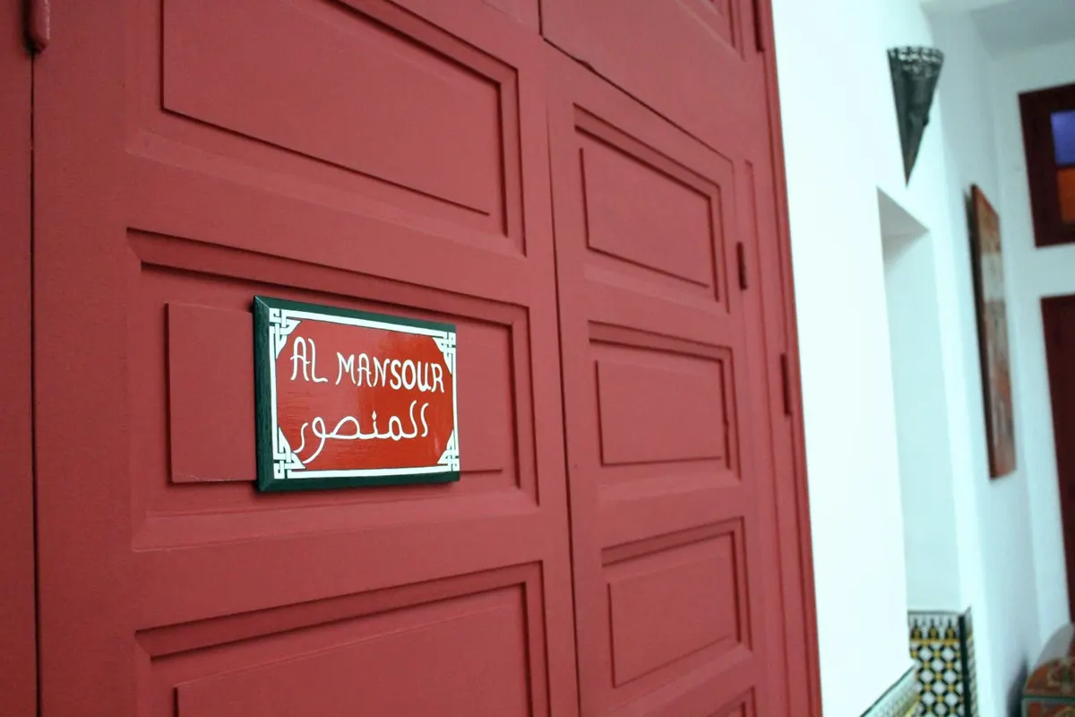 The lacquered red door of Al Mansour with its bilingual plaque