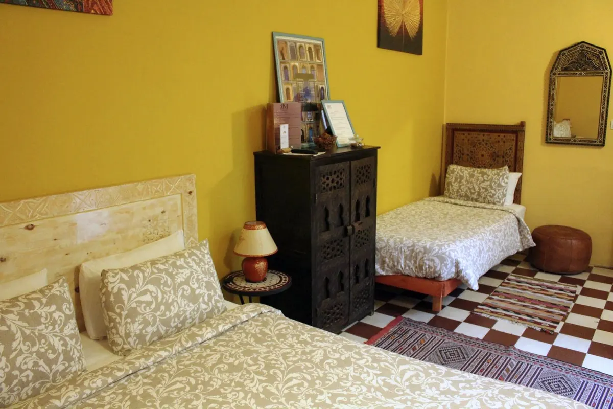 Chellah room: queen and single beds, ochre walls, carved chest
